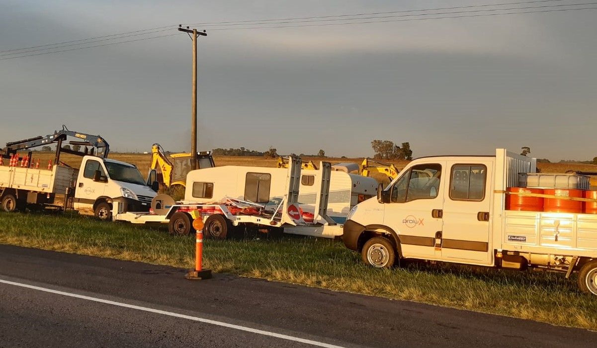 Camiones con hidrogrúa, acoplado y retroexcavadora estacionados junto a una ruta