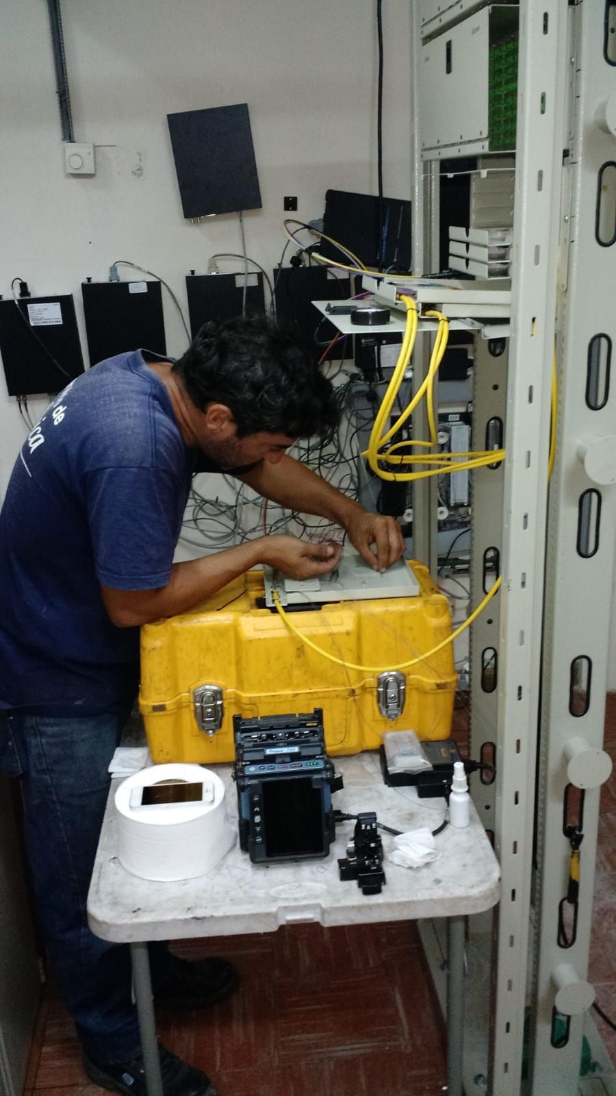 Técnico fusionando fibra óptica con una empalmadora junto a un rack de telecomunicaciones