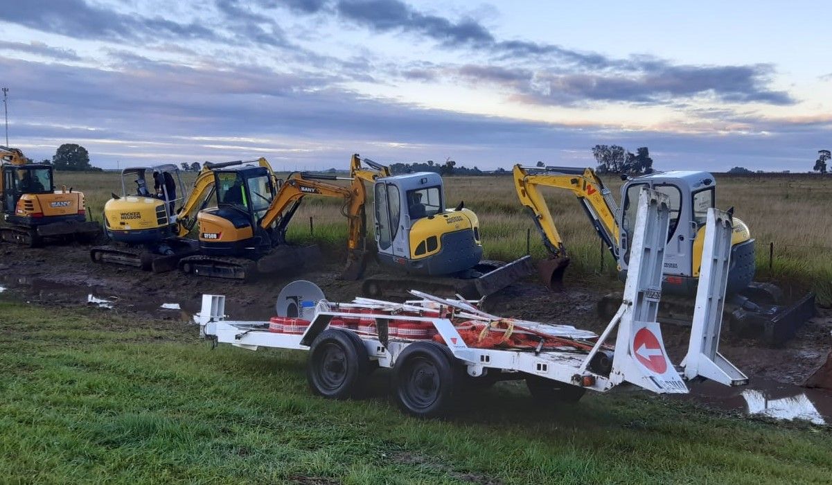 Cuatro miniexcavadoras y un acoplado de señalización en un campo al amanecer